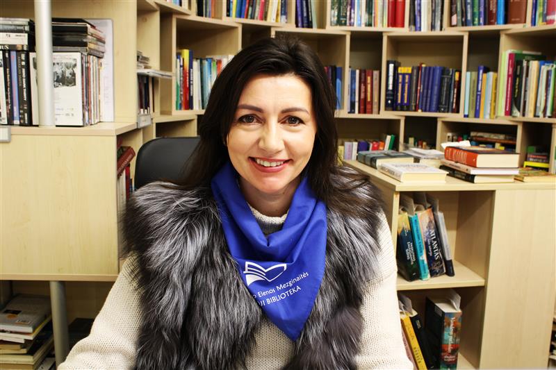 Besišypsanti bibliotekos darbuotoja knygų fone