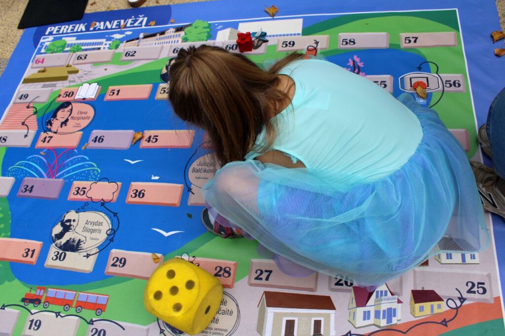 Mergaitė atsitūpusi žaidžia žaidimą su domino kauliuku