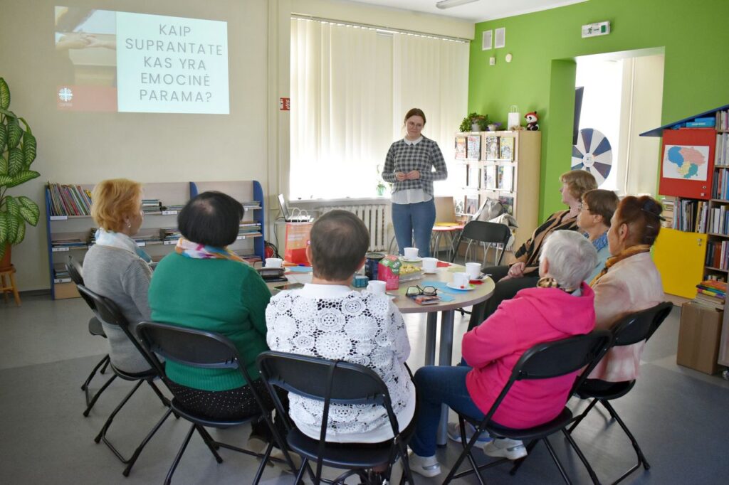 Ratu susėdę moterys klausosi stovinčios moters