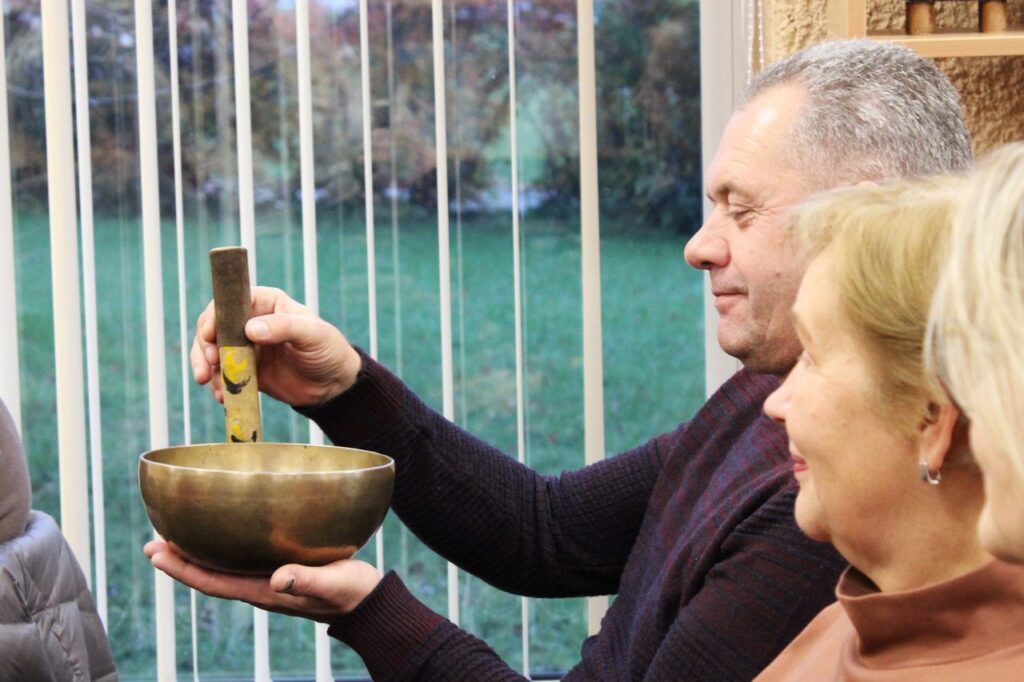 Šalia sėdi vyras ir moteris. Vyras laiko dubenį