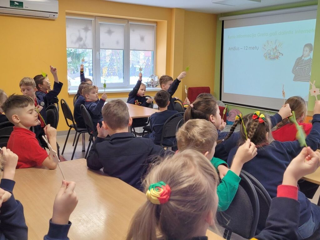 Vaikai, iškėlę rankas, sėdi prieš projektoriaus ekraną