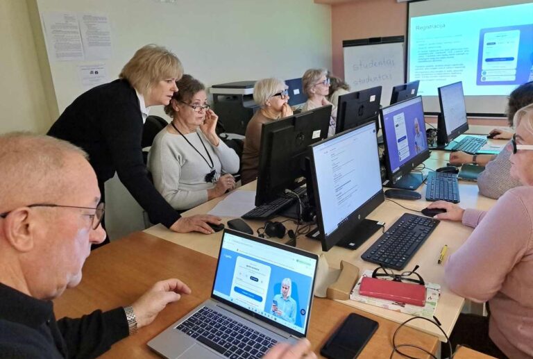 Moteris padeda prie kompiuterių dirbantiems senjorams